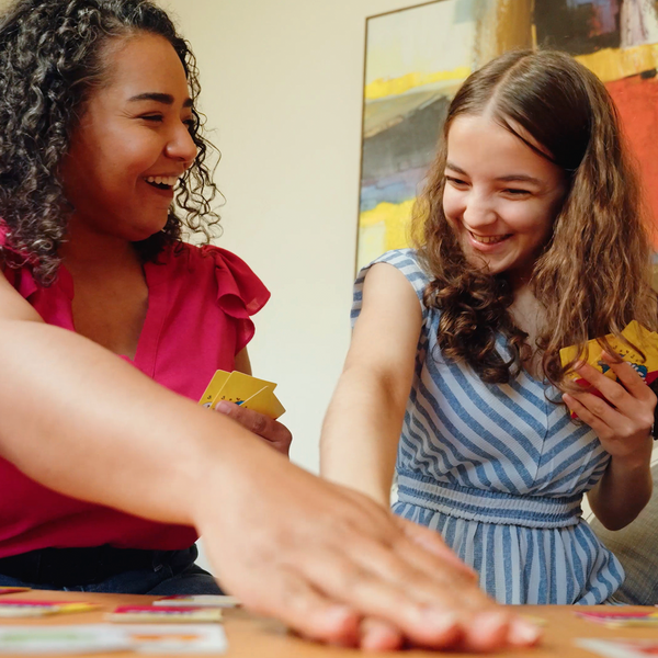 Two women playing a board game together with a colorful abstract painting in the background.
