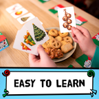 A person holds two illustrated cards over a table with cookies and game pieces. One card shows a Christmas tree and ornaments, and the other shows a string of bells.