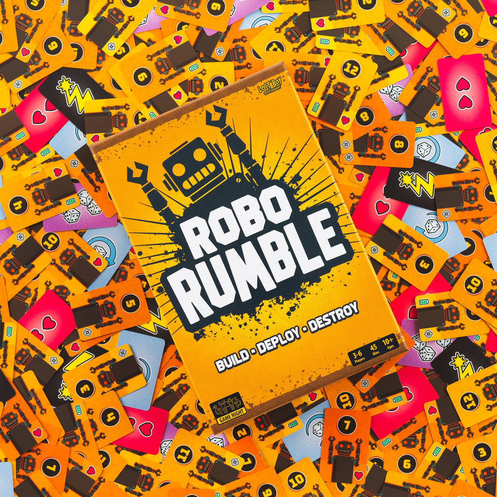 The board game 'Robo Rumble' box is shown at an angle, surrounded by a dense pile of colorful game cards featuring robot and tech designs. The box is bright orange with bold white and black text, and the background is a colorful mix of orange, yellow, pink, and blue cards. game night family fun
